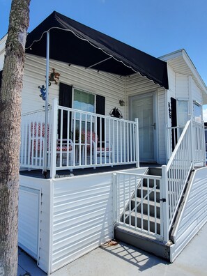A white mobile home with a black awning, a porch with a white railing, and a staircase leading to the entrance. - Cozy vacation home (Jensen Beach)