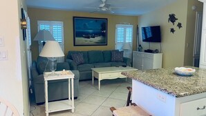 A living room with a sofa, coffee table, and a TV. There is a ceiling fan and a painting on the wall. - Cozy vacation home (Jensen Beach)