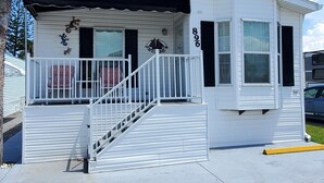A white single-story building with a black awning, a small porch with a railing, and a number '896' on the side. - Cozy vacation home (Jensen Beach)
