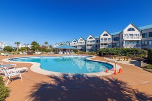 A swimming pool surrounded by lounge chairs and a building with multiple balconies. - Ocean View Beachfront +In/Outdoor Pools + Sauna! (Gulf Shores)