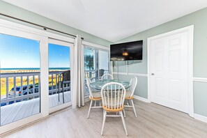 A balcony with a glass table and chairs, a TV mounted on the wall, and a view of the sea. - Ocean View Beachfront +In/Outdoor Pools + Sauna! (Gulf Shores)