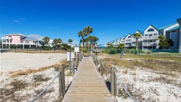 A wooden boardwalk leading to a beachfront hotel with multiple balconies and palm trees.