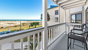 A balcony with a view of the beach, a glass table, and two wicker chairs.