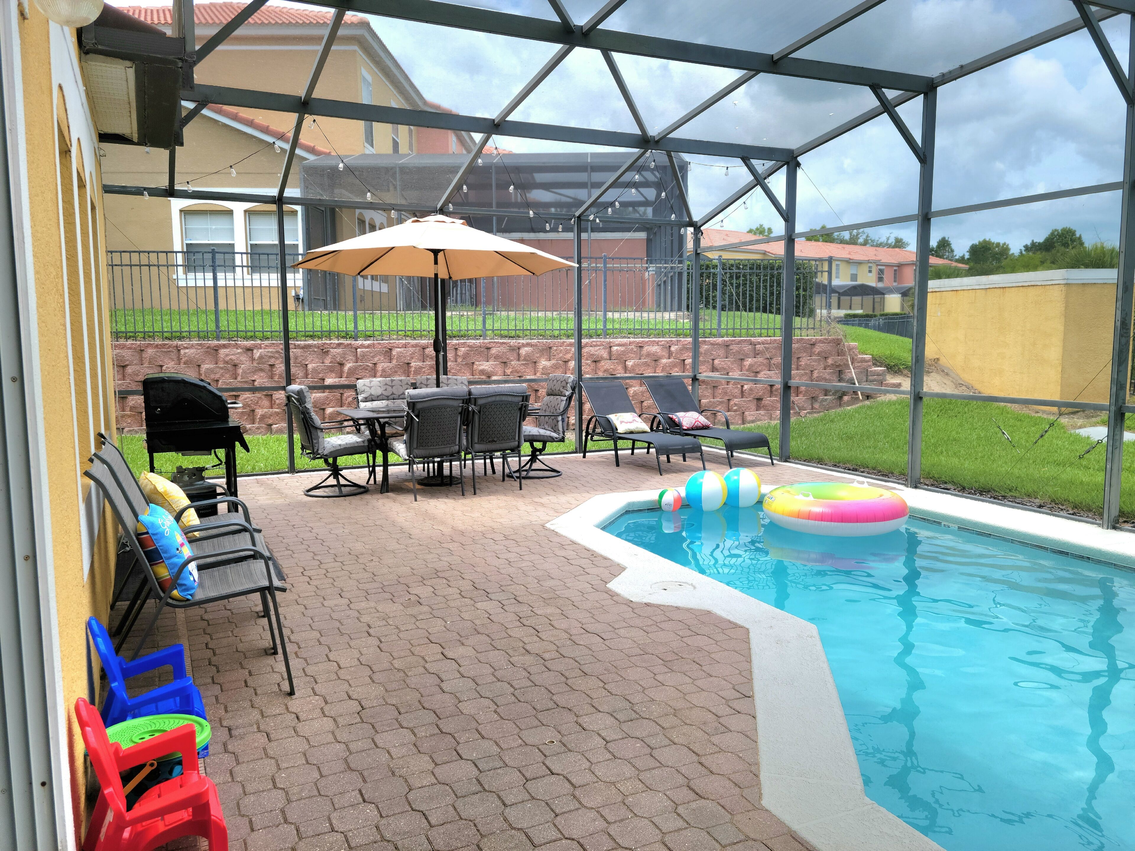 An outdoor patio with a pool, covered seating area, and a grill.