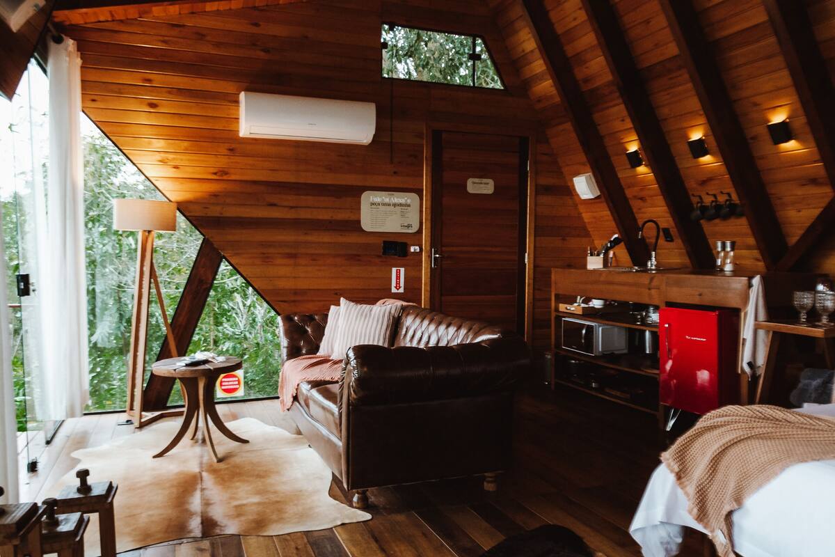 A cozy cabin interior with a wooden ceiling, a leather sofa, a small table, and a red refrigerator.
