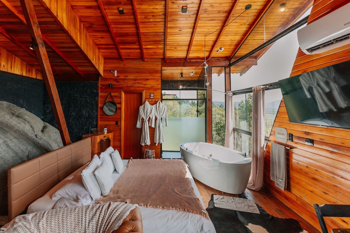 A wooden cabin bedroom with a large bed, a bathtub, and a television.