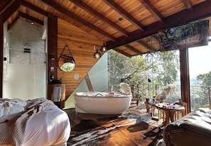Un interior moderno con techo de madera, una bañera grande, un sofá y vistas a árboles.