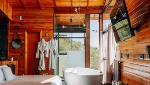 Interior de una cabaña de madera con una bañera grande, una cama y un comedor.