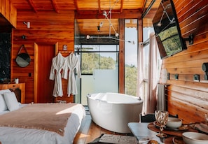 A wooden cabin interior with a large bathtub, a bed, and a dining area. - Vale dos Saltos Chalés (Tijucas)