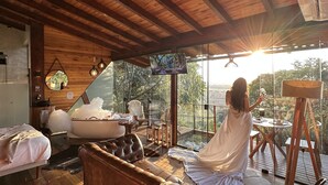 Una habitación con techo de madera, una cama, un sofá, una bañera y un ventanal con vistas.