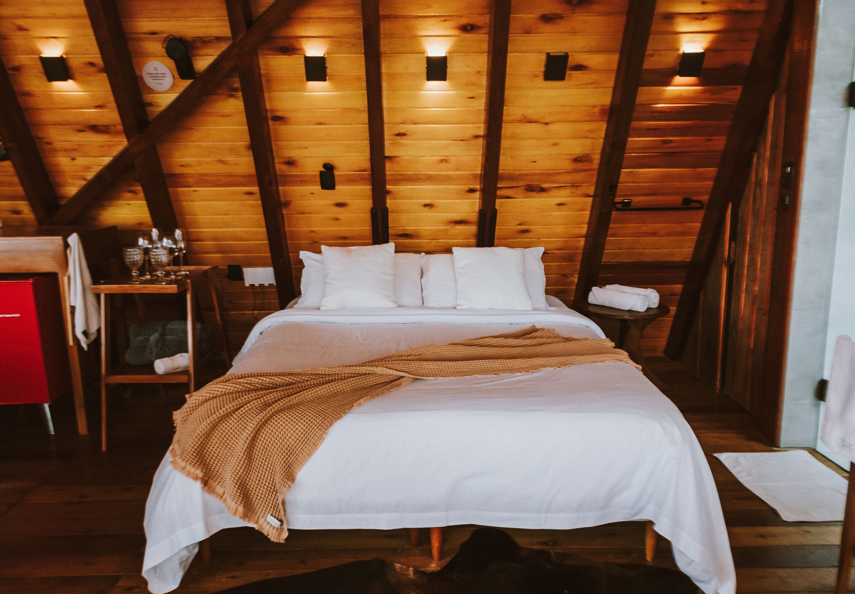 Una habitación con paneles de madera, una cama, un armario rojo e iluminación instalada en la pared.