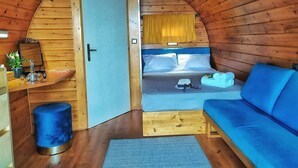 L’intérieur d’un chalet accueillant, avec un plafond en bois, un lit avec une literie bleue, un canapé bleu et une petite table agrémentée d’un miroir et d’objets décoratifs.