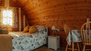 A cozy wooden cabin room with a bed, a small table, and a chair. - Glamping in Wiltshire the Green Knoll is a charm (Chippenham)