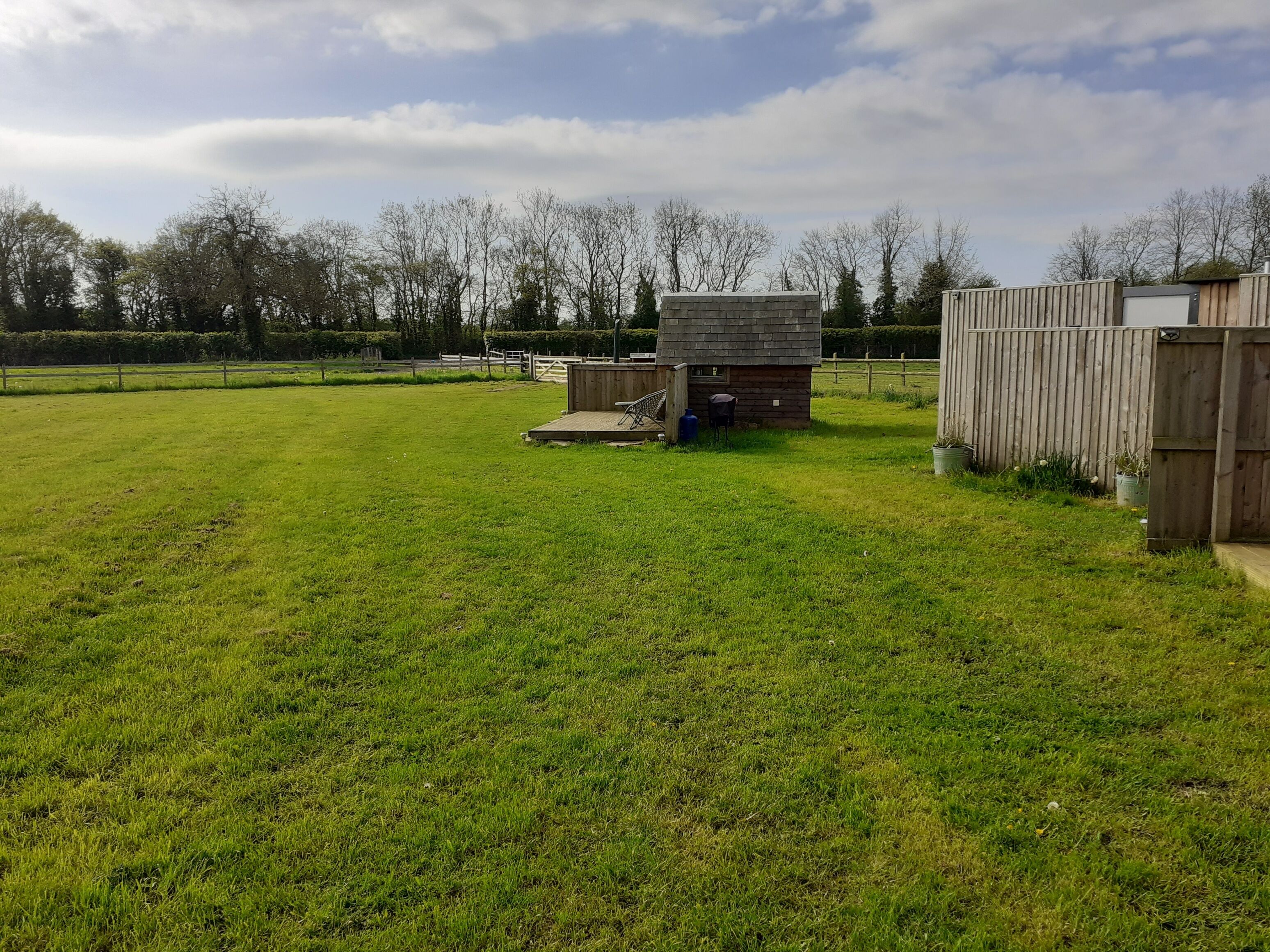 A grassy field with a small wooden structure, possibly a shed or storage unit, and a wooden fence.