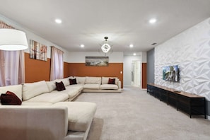 A modern living room with a sectional sofa, a coffee table, and a TV on a wall with a geometric pattern.