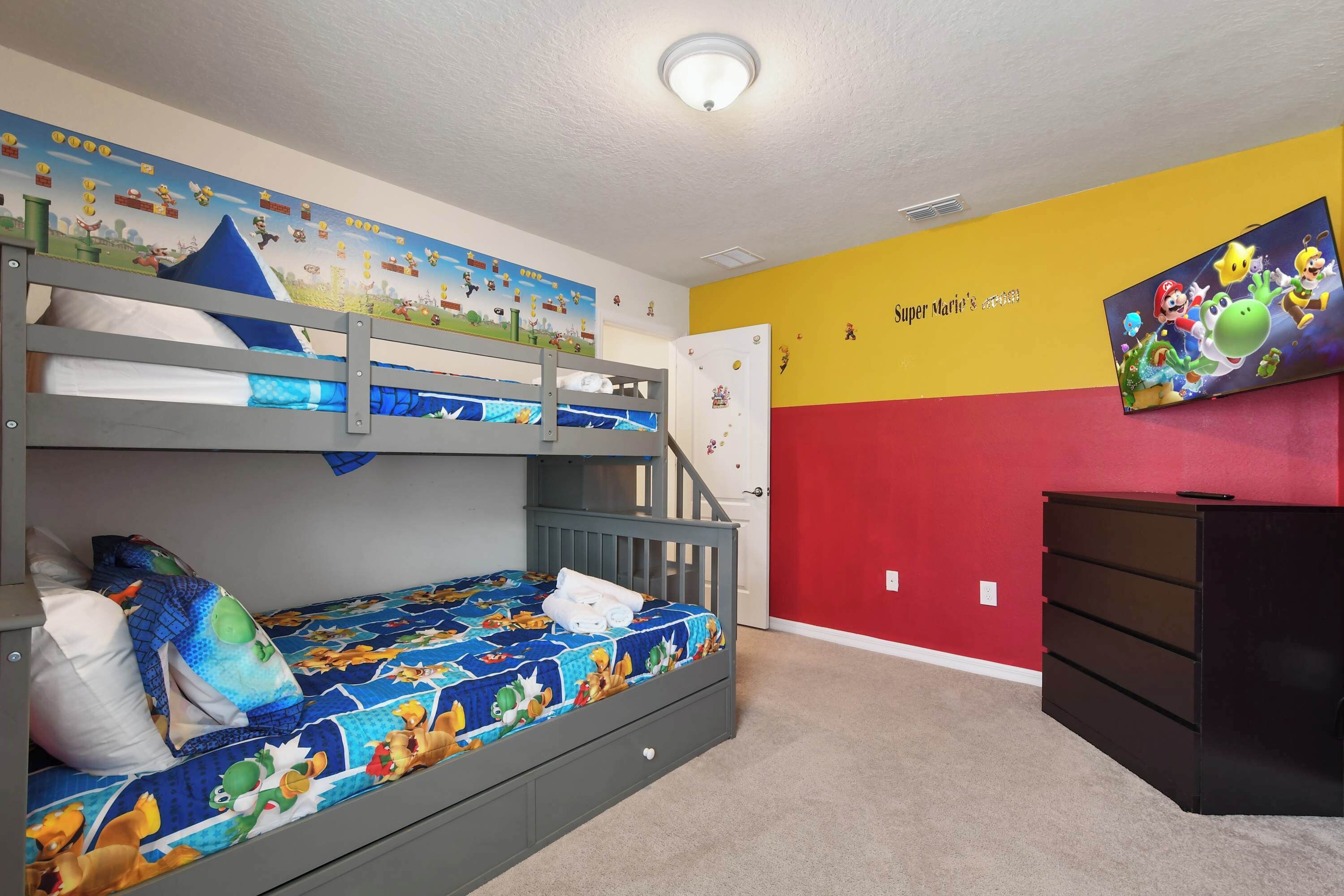 Ein Kinderzimmer mit Etagenbetten, Wandmalerei, Flachbildfernseher und Kommode.