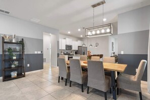 A modern kitchen with white cabinets, stainless steel appliances, and a dining area with a wooden table and grey upholstered chairs. - Solterra Villa | Private Pool, Games & Themes (Davenport)