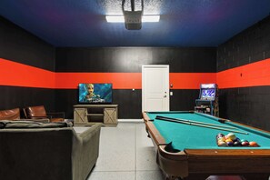 A pool table with balls, a television, and a video game console in a room with black and orange walls. - Solterra Villa | Private Pool, Games & Themes (Davenport)
