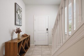 Ein Flur mit einer weißen Tür, einem Holzkonsolentisch mit Vase und Pflanze sowie einer Treppe mit weißen Geländern.