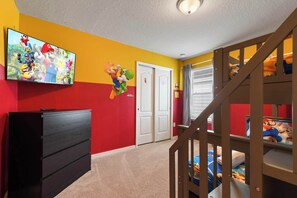A room with a TV on the wall, a dresser, a door, and a staircase.
