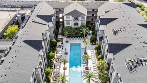 Een hoog hotel met een centraal gelegen zwembad, omringd door ligbedden en palmbomen.