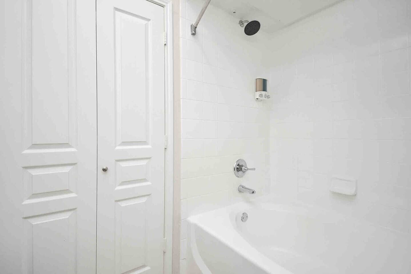 A bathroom with a white bathtub, a shower, and a white door with a handle.