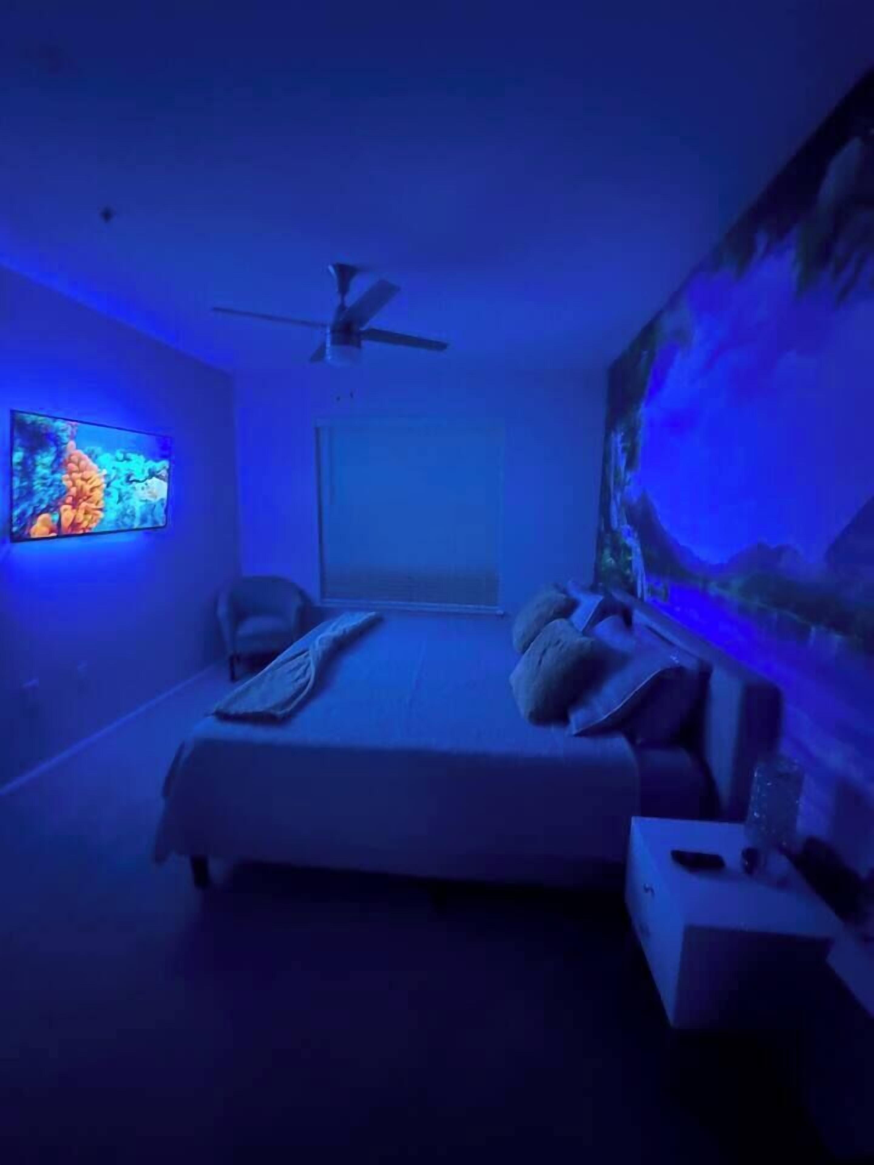 Un dormitorio con cama, ventilador de techo, televisor en la pared y un acuario.
