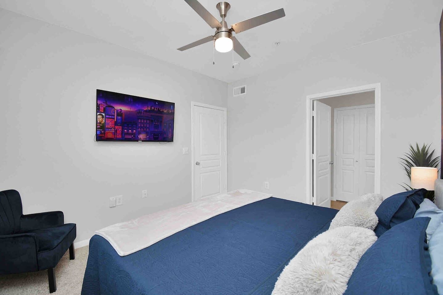 A bedroom with a bed, a ceiling fan, a wall-mounted TV, and two doors.
