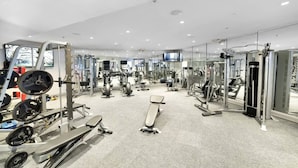 Een moderne sportschool met diverse fitnessapparaten, een grote spiegel en een televisiescherm.