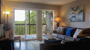 Un salon comprenant un canapé, une table basse, une lampe et une vue sur une terrasse extérieure, accessible par une porte-fenêtre coulissante.