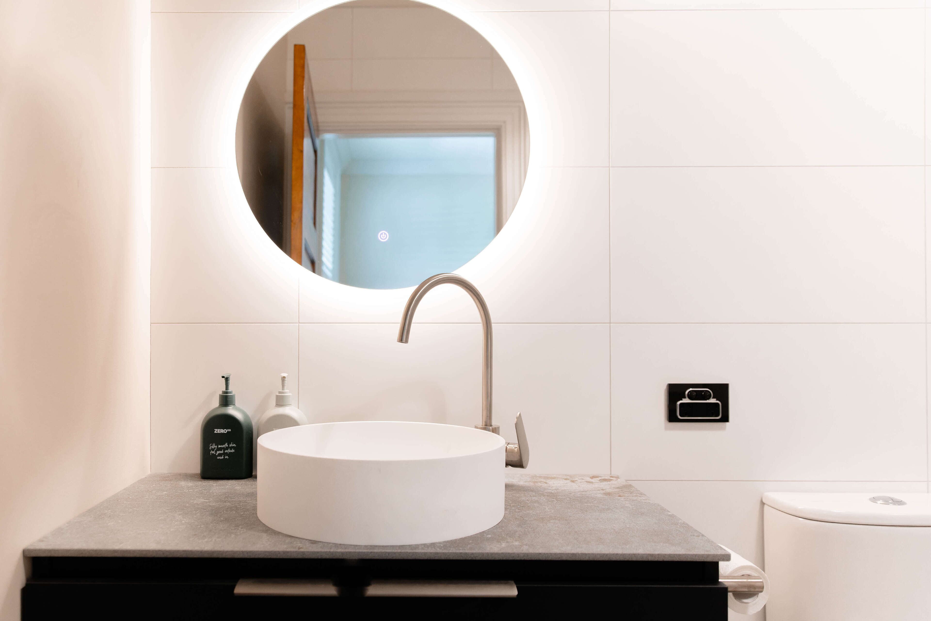 A bathroom with a round mirror, a white sink, and a toilet.