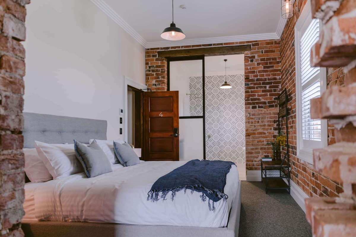 A bedroom with a large bed, a wooden door, brick walls, and a hanging light fixture.