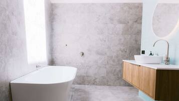 Un baño moderno con una bañera independiente, un tocador de madera y un espejo grande.