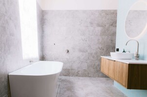 Un baño moderno con una bañera independiente, un tocador de madera y un espejo grande.
