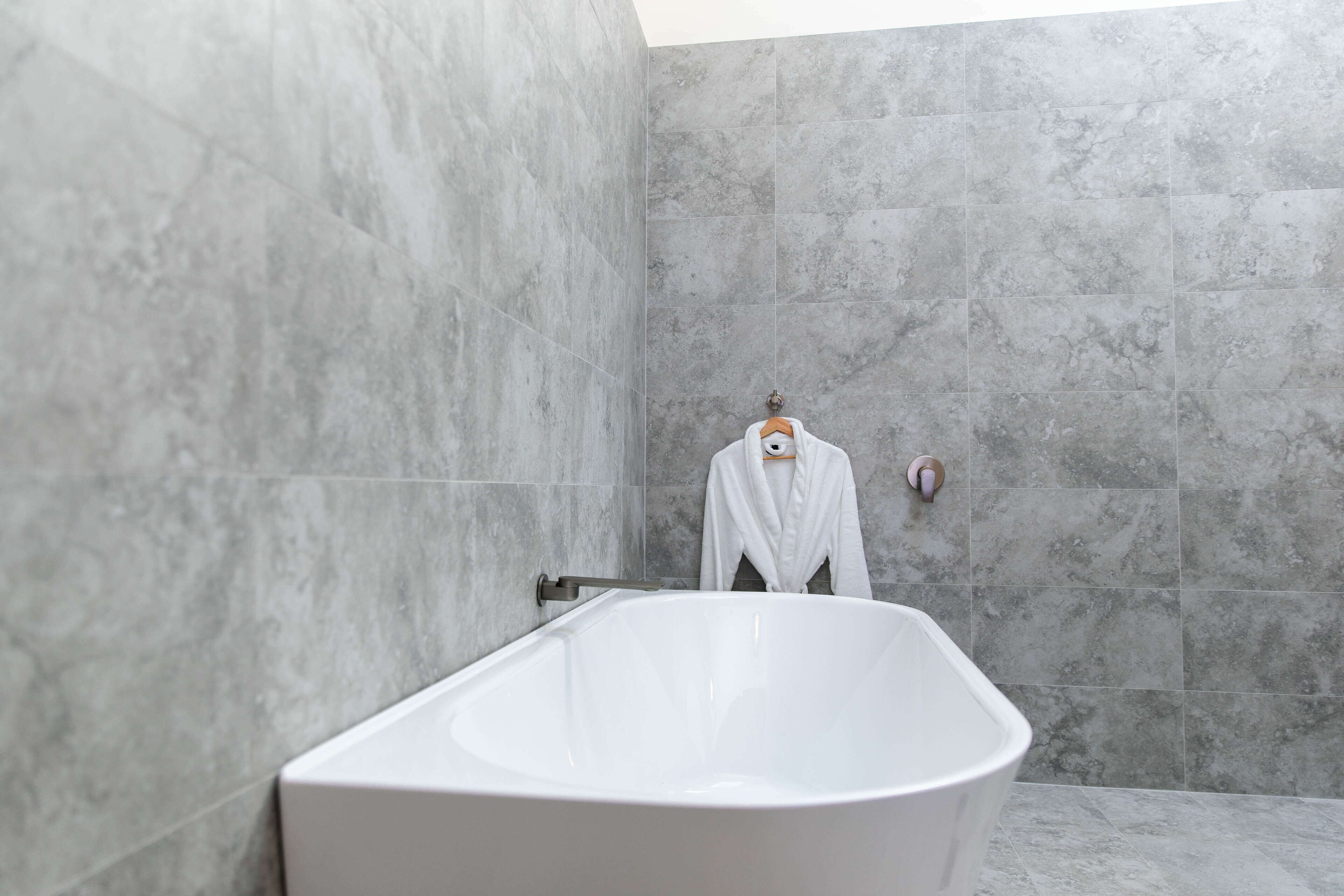 Un baño moderno con una bañera independiente, baldosas de mármol gris y un perchero con una toalla blanca.