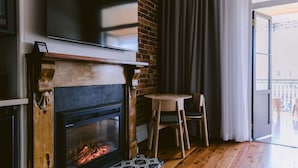 Una sala de estar moderna con chimenea, un televisor de pantalla plana montado sobre ella, una mesa redonda de madera y vistas al exterior a través de un gran ventanal corredizo.