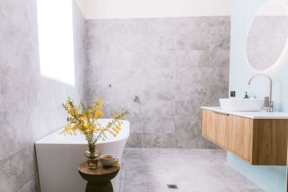 A modern bathroom with a freestanding bathtub, a wooden vanity, and a vase with yellow flowers on a pedestal.