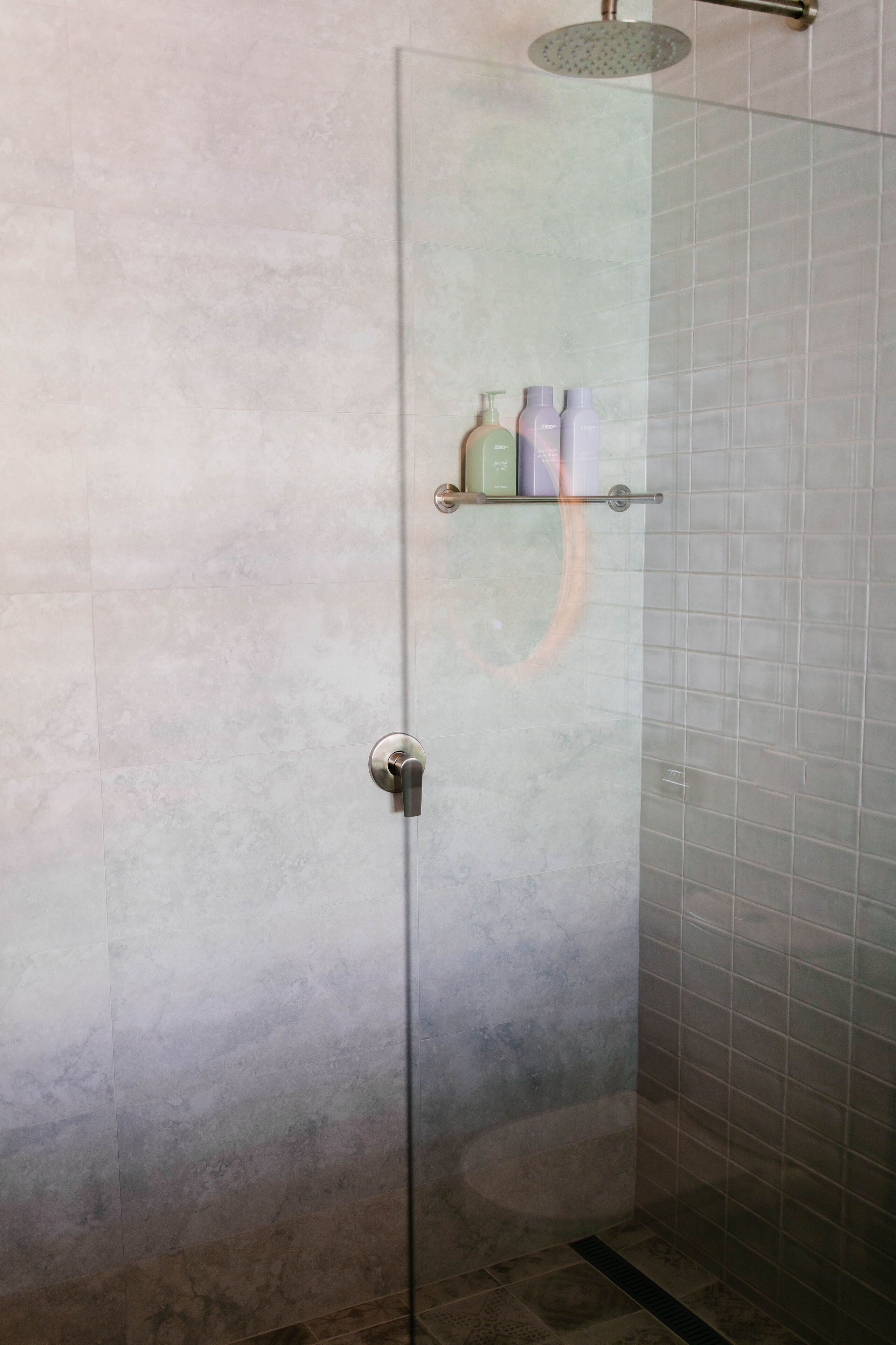 A glass-enclosed shower with a shelf holding toiletries.