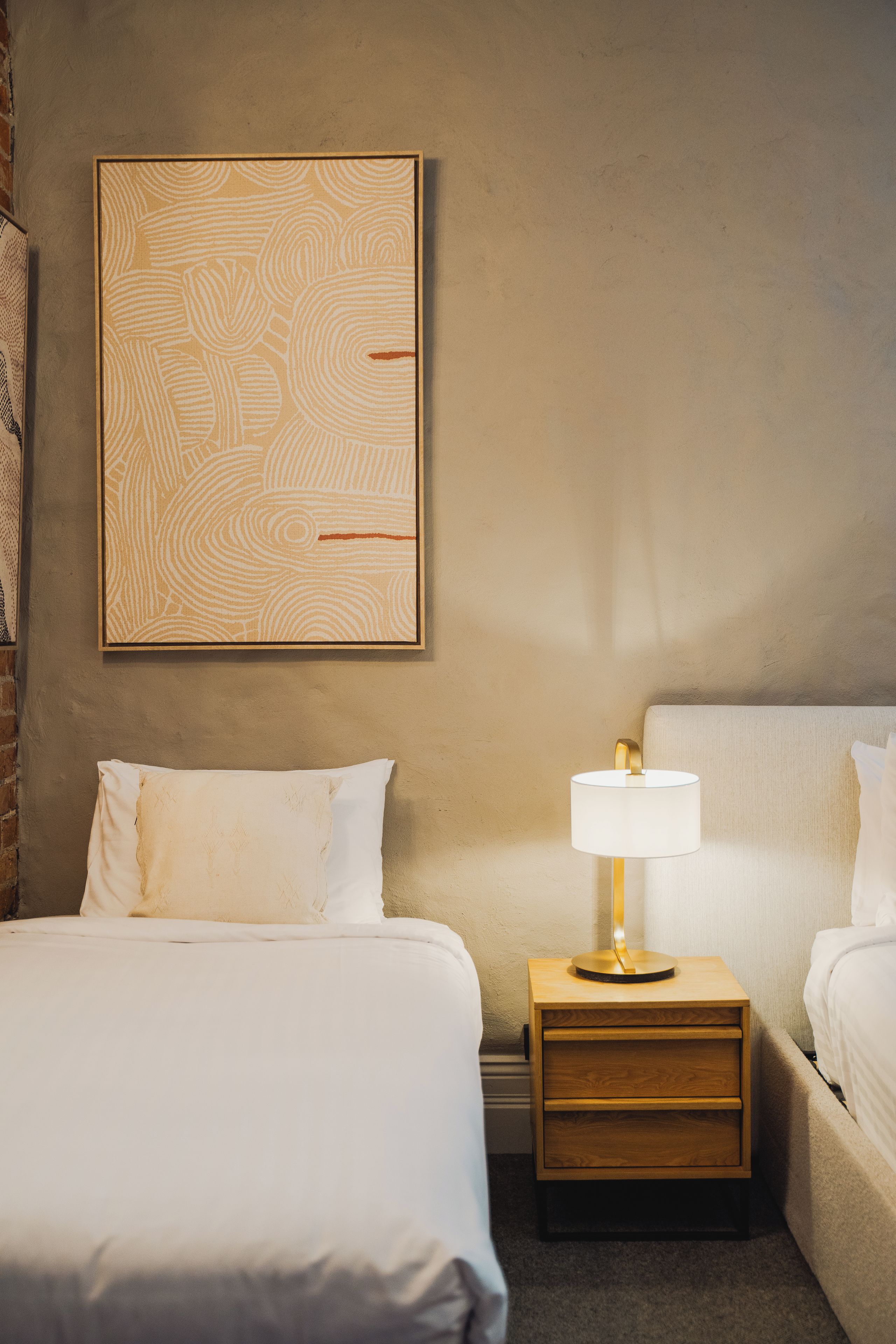 A hotel room with a large abstract painting, a bedside lamp, and a neatly made bed.