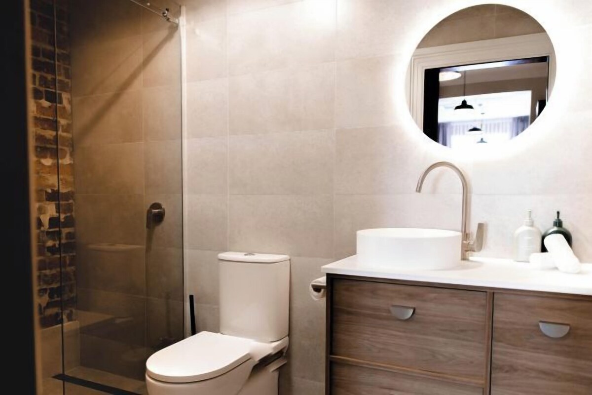 Un baño moderno con ducha de vidrio, inodoro y tocador con lavabo y espejo.