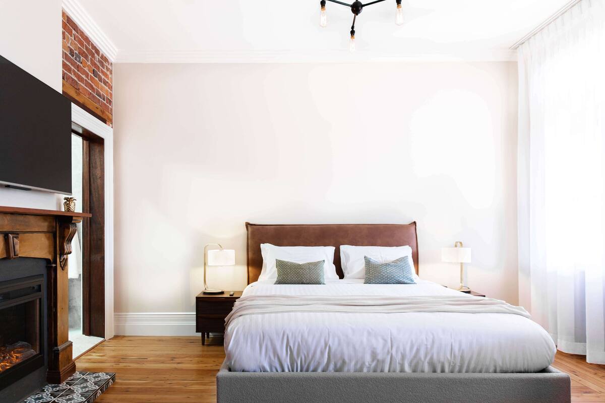 A bedroom with a large bed, a fireplace, and a TV mounted on the wall.