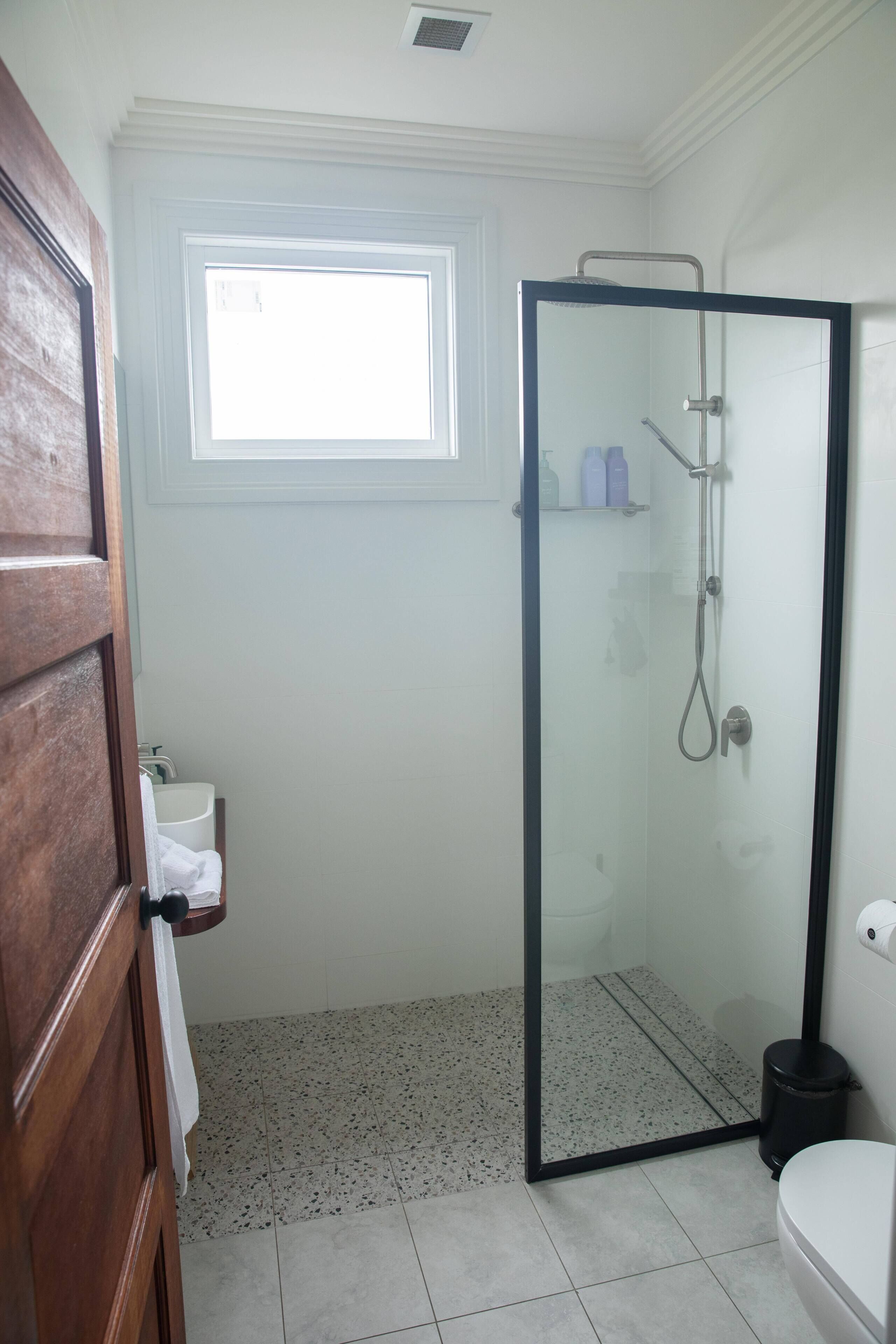 Un bany amb dutxa amb envàs de vidre, un vàter, un lavabo i una finestra que deixa entrar llum natural.