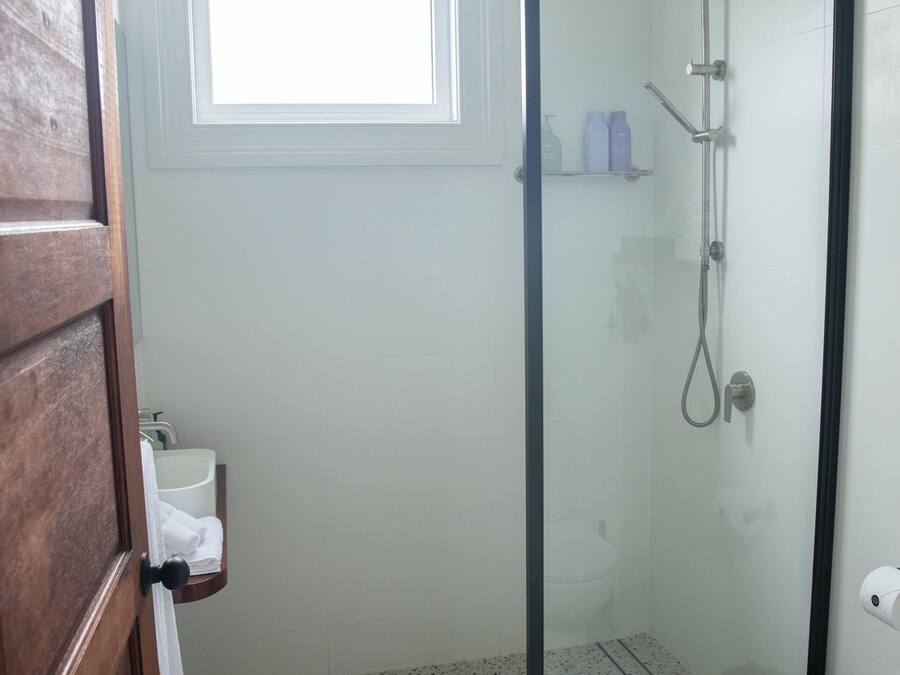 Un bany amb dutxa amb envàs de vidre, un vàter, un lavabo i una finestra que deixa entrar llum natural.