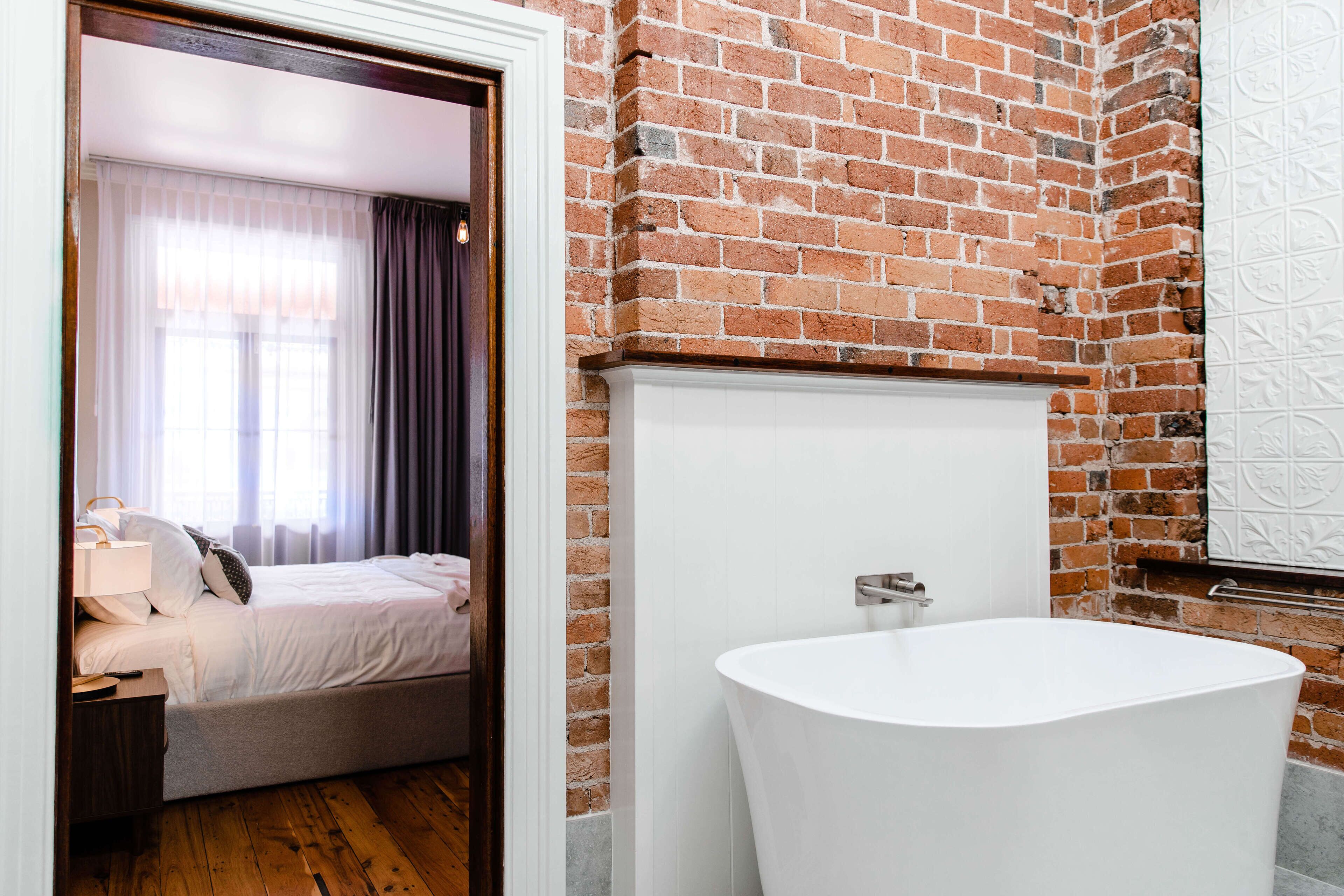 A room with a brick wall, a white bathtub, and a bed with a wooden headboard.