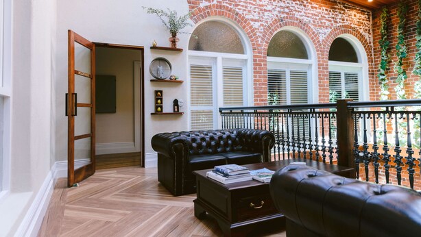 Una sala de estar con un sofá de cuero negro, una mesa de centro de madera y una pared de ladrillo con ventanas de arco.