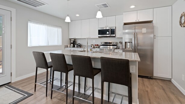 A modern kitchen with a central island, bar stools, stainless steel appliances, and pendant lighting.