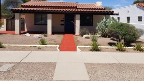 A single-story house with a red-tiled roof, a covered porch, and a red pathway leading to the entrance.