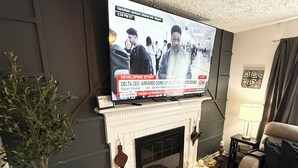 Ein Wohnzimmer mit einem Flachbildfernseher über einem weißen Kamin, einer Topfpflanze und einem Sofa.