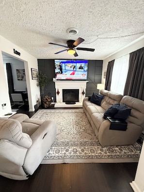 A living room with a fireplace, a television, a ceiling fan, and a sofa.