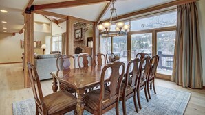 A dining area with a wooden table and chairs, a chandelier, and a view of a snowy landscape through large windows.